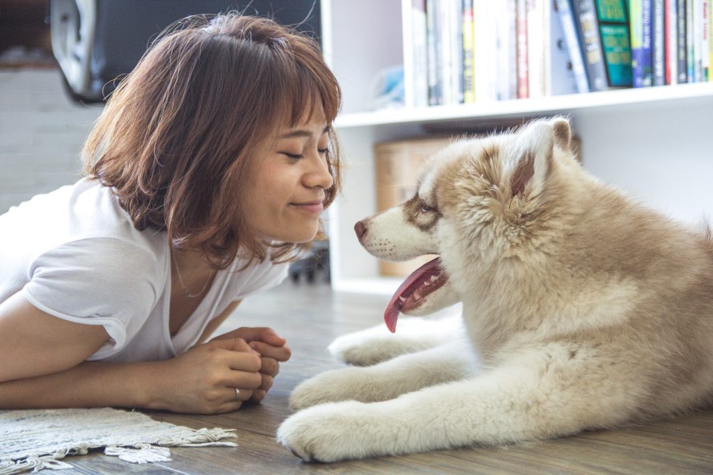 アジア系の女性と犬が顔を見合わせて笑っている。